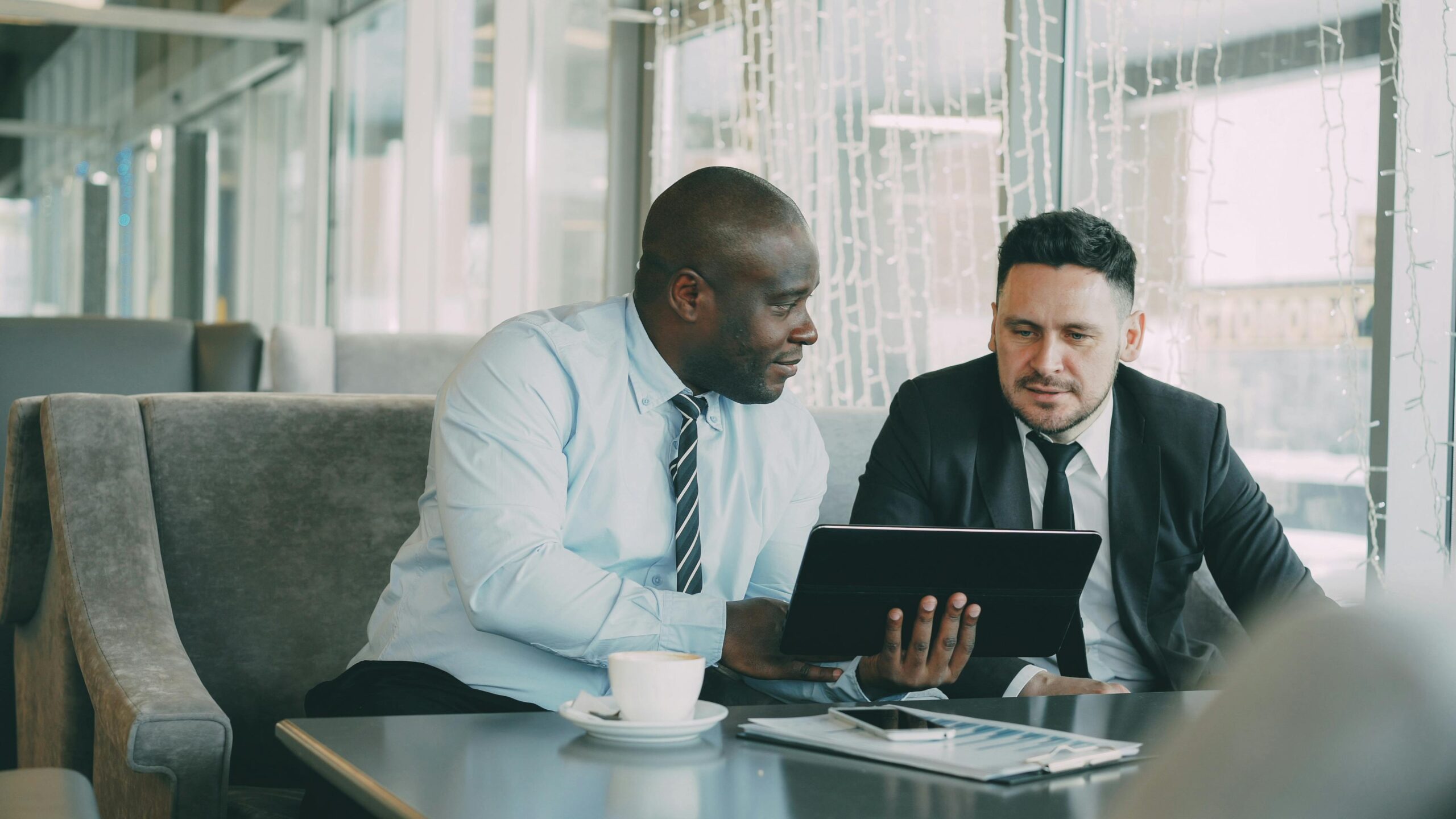Two men in business attire collaborating over a tablet in a modern office setting.